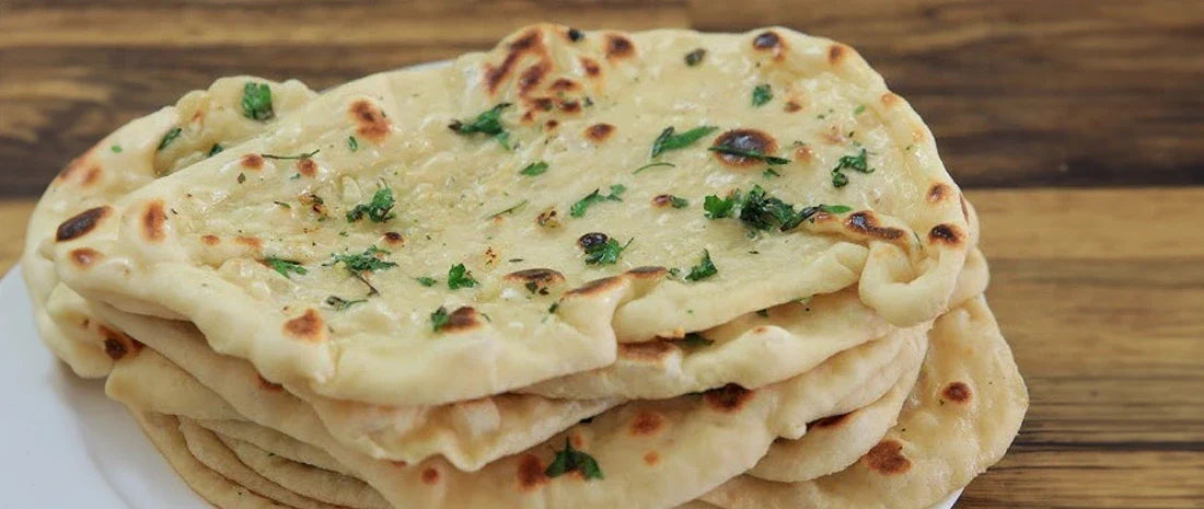 Stack of homemade garlic naan bread with fresh coriander and charred spots on wooden cutting board