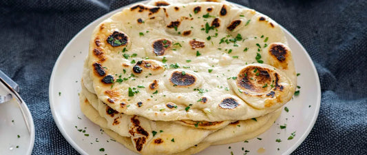 Stack of homemade naan bread with charred spots and fresh parsley garnish on a white plate