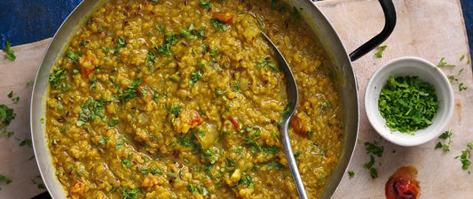 Traditional dal (lentil curry) cooking in a stainless steel pan with fresh coriander and spices, served with a small bowl of chopped herbs on the side