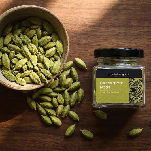 Green cardamom pods in a bowl and jar on a wooden surface