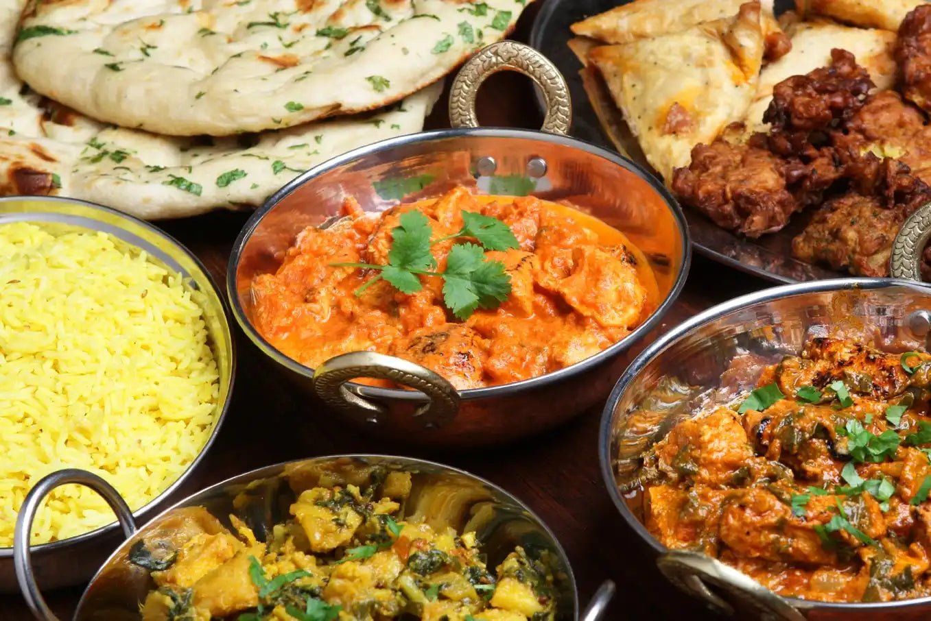 Traditional homemade Indian food spread featuring butter chickekn with naan bread, saffron rice, and authentic spices served in copper bowls