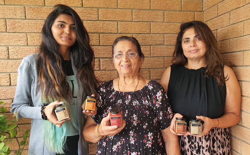 Three of our family members standing in front of a brick wall, each holding jars featuring our Indian spices when the business was launched.