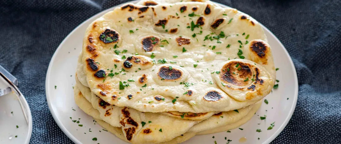 Stack of homemade naan bread with charred spots and fresh parsley garnish on a white plate