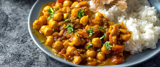A bowl of spiced chickpea curry served alongside white basmati rice, garnished with fresh green herbs and golden turmeric-infused sauce