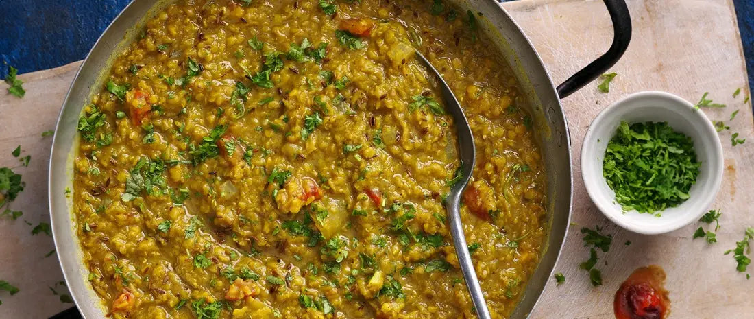 Traditional dal (lentil curry) cooking in a stainless steel pan with fresh coriander and spices, served with a small bowl of chopped herbs on the side
