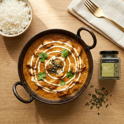 Dish of butter chicken with a side of rice on a wooden table, garnished with coriander and kasoori methi.