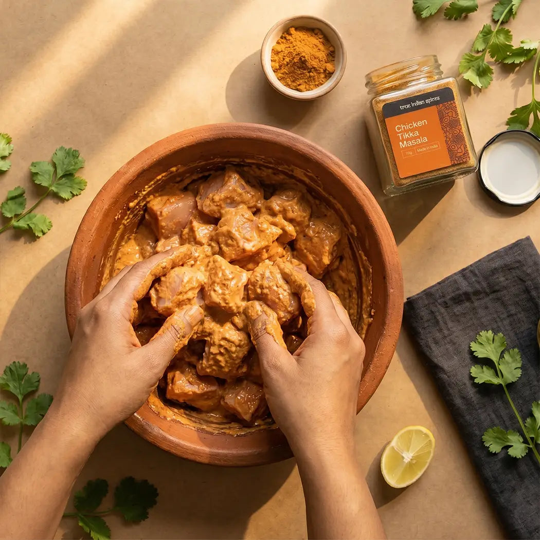 Hands mixing marinated chicken in a bowl with spices and herbs on a wooden surface