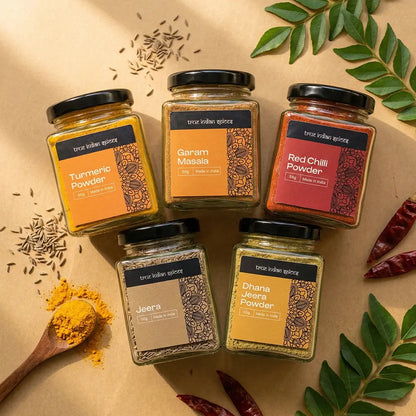 Five jars of spices on a beige background with herbs and spices around