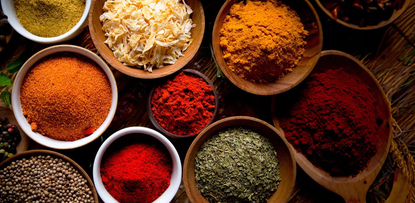 Colourful Indian spices in bowls - turmeric, chilli powder, garam masala, cumin seeds & herbs arranged on dark surface